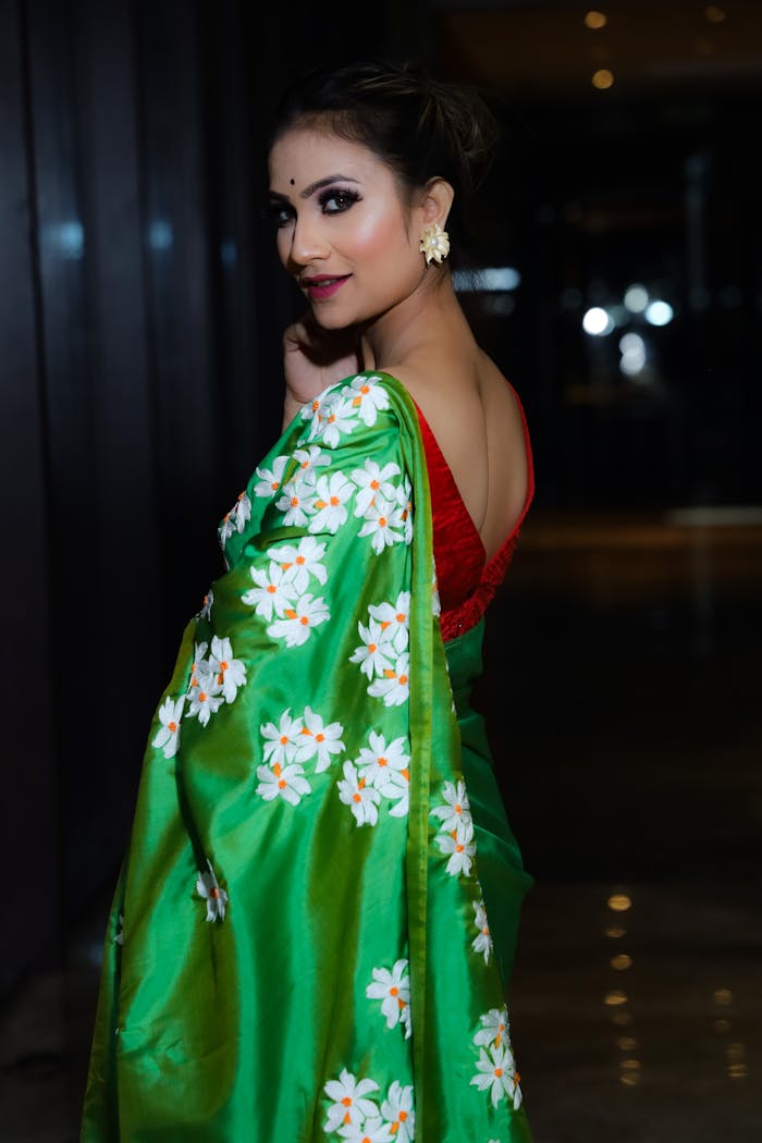 A woman in a vibrant floral saree poses gracefully indoors, exuding traditional style and elegance.